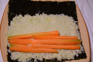Hoja de sushi con arroz encima y zanahoria en palitos
